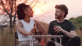 Young diverse couple enjoying a romantic date, toasting with beer bottles and laughing together outdoors during a beautiful golden hour - Powered by Shutterstock - Get 15% off with code: PIKWIZARD15