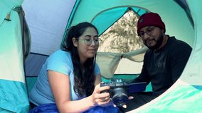 Man and woman enjoying a relaxing camping day in the forest as they look at photos on a digital camera. The couple stands beside their tent, smiling and sharing a joyful outdoor moment. - Powered by Shutterstock - Get 15% off with code: PIKWIZARD15