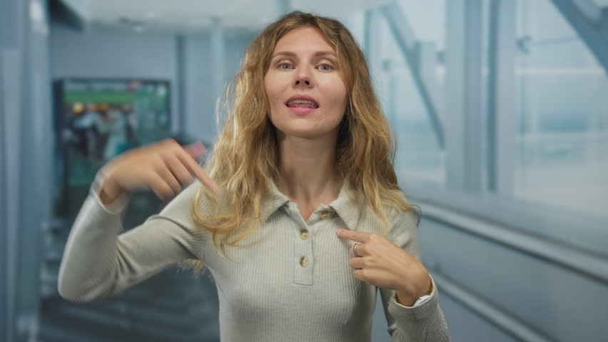 Woman lifts hand waving inside airport as blonde young figure worried calling out across a terminal hallway.
