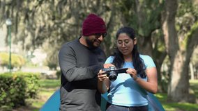 Smiling couple looking at the photos they took on a digital camera while camping in a forest. They stand near their tent, enjoying nature and the outdoors together. - Powered by Shutterstock - Get 15% off with code: PIKWIZARD15