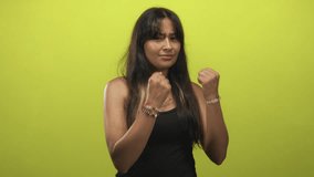 Young latina brunette woman throwing a punch with fists raised in a lime green studio wearing a black tank top; confidence empowerment. - Powered by Shutterstock - Get 15% off with code: PIKWIZARD15