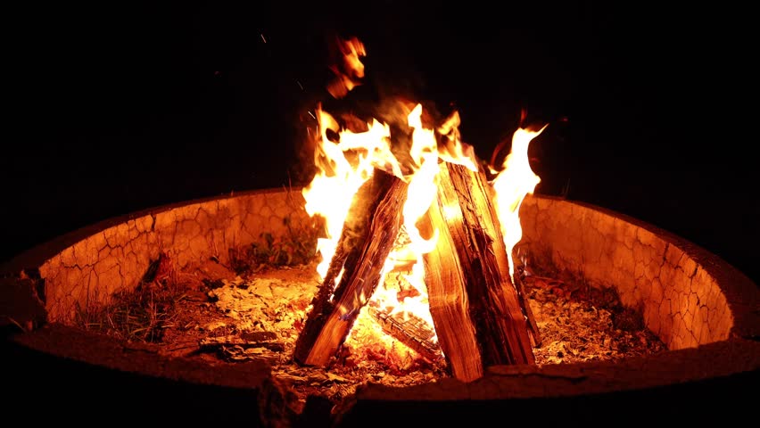 Footage of a campfire arranged in a teepee structure burning in a round fire pit.