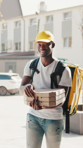 A smiling delivery man wearing a yellow cap and holding a pizza box, ready to deliver a delicious pizza to the customer.