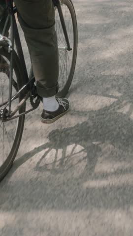 Vertical detail shot showing the shadow of bicycle wheels spinning along a sunny forest road. Calm movement, soft light, and asphalt texture create a mindful rhythm of summer travel. High quality 4k