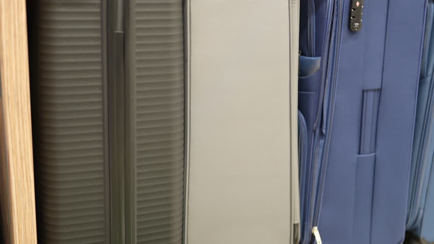Various suitcases are shown in a row at a store. Colors include blue, grey, teal, black, and red. They are lined up and ready for purchase for your next trip.