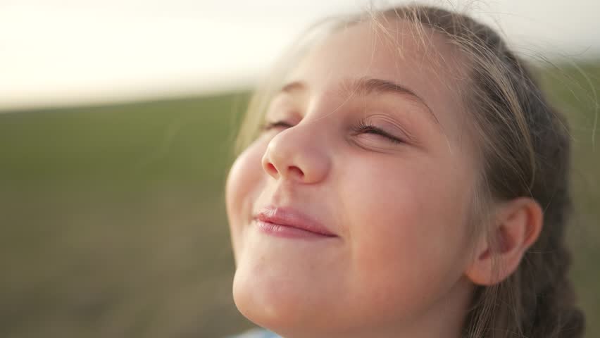 Young girl smiles with peaceful joy while child looks upward in field of grass showing smile and nature happiness under soft sunlight with wind in hair portrait of joyful girl enjoying outdoor play