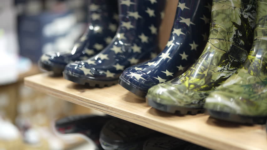 Colorful rain boots line a wooden shelf. Boots feature designs such as stars, camouflage, and solid black. Perfect for puddle jumping on a wet day in any town.
