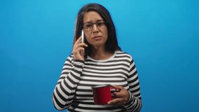 Woman middle aged brunette holding red mug and smartphone to ear while listening in studio; pensive reflection. - Powered by Shutterstock - Get 15% off with code: PIKWIZARD15