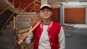 Young man in baseball uniform with bat indoors at construction site playfully pointing at his nose showcasing casual interaction in unique setting blending sports and urban elements. - Powered by Shutterstock - Get 15% off with code: PIKWIZARD15