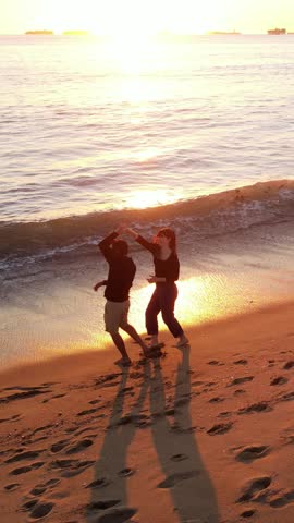 Aerial shot of a happy couple walking on the beach at sunset in Southern California. Vertical Video.