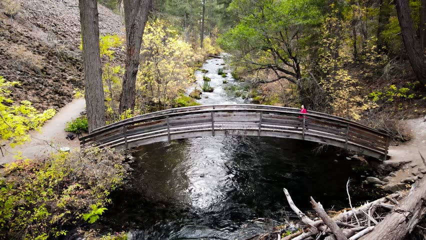 Aerial shot of a Asian female hiker walking across a bridge over Burney Creek in Northern California.