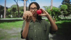 Young hispanic woman holding brain model in one hand and a red heart in the other in forest; contemplation balance. - Powered by Shutterstock - Get 15% off with code: PIKWIZARD15