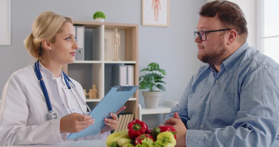 Nutritionist leads a healthcare clinic consultation, reviewing diet with a fat overweight patient and discussing obesity risks, and advice for wellness. Doctor guides patient on diet today.