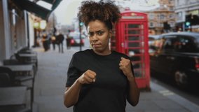 Woman with fists raised in a street boxing pose by a red phone booth and black taxi, grimacing in defense; urban defiance. - Powered by Shutterstock - Get 15% off with code: PIKWIZARD15