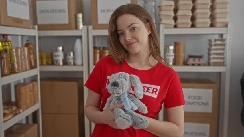 Volunteer woman smiling holds gray bunny with hands in building donation center; charity compassion.