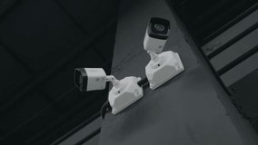 Low-angle arc shot of two digital CCTV surveillance cameras mounted on wall, recording routine activity in garage or industrial warehouse, no people. - Powered by Shutterstock - Get 15% off with code: PIKWIZARD15