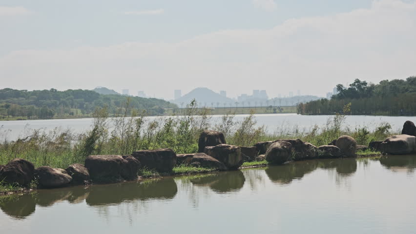 A Cinematic Wide Shot of Wetland Park Lake, Featuring Rocky Piles in the Water, Distant Shoreline, and Far Mountains (ProRes 422)