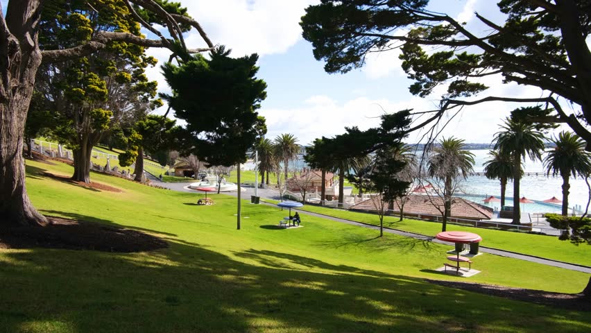 Serene parkland at Eastern Beach Reserve in Geelong, Victoria, Australia, with scattered picnic tables, a public swimming pool, and the waterfront in the background. A relaxing and inviting atmosphere