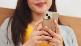 Asian young woman holding smartphone and smiling while sitting bed relaxed mood casual indoor scene and holding smartphone bed using mobile device with relaxed expression warm lighting while smiling - Powered by Shutterstock - Get 15% off with code: PIKWIZARD15