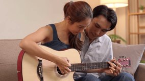 Happy young Asian man woman bond playing acoustic guitar indoors at home. Learning new instrument together romantic hobby. - Powered by Shutterstock - Get 15% off with code: PIKWIZARD15