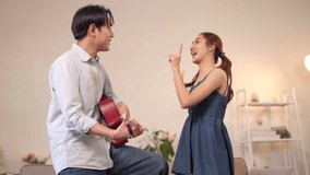 Joyful Asian couple share music bond at home. Adult man plays guitar for happy woman clapping in cozy living room. Romance lifestyle. - Powered by Shutterstock - Get 15% off with code: PIKWIZARD15