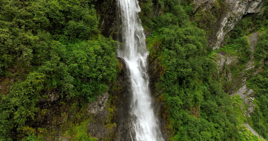 Water hits the rock as falls from the height. View on the waterfall in the green mountains. Alaska, USA.