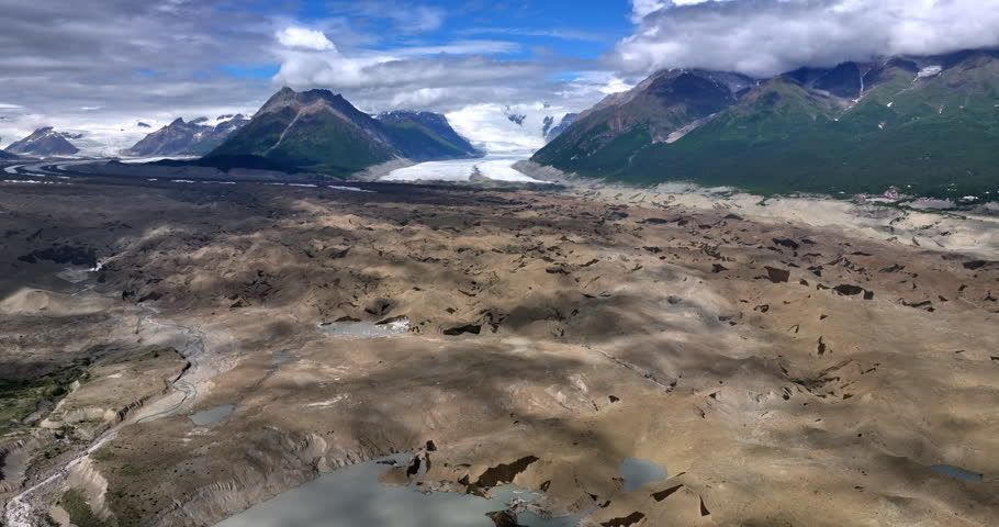 Vegetation less rocky landscape with some water from melting ice. Striking rocks coated with clouds at backdrop. Alaska, USA. Aerial view.
