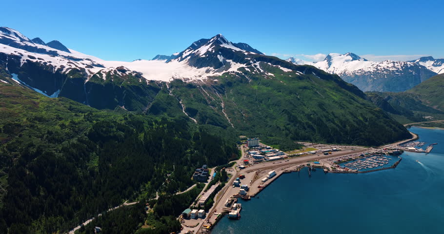 Approaching the beautiful small town located in the verdant mountains. Snow lying on the rocks reflects sunlight. Alaska, USA.