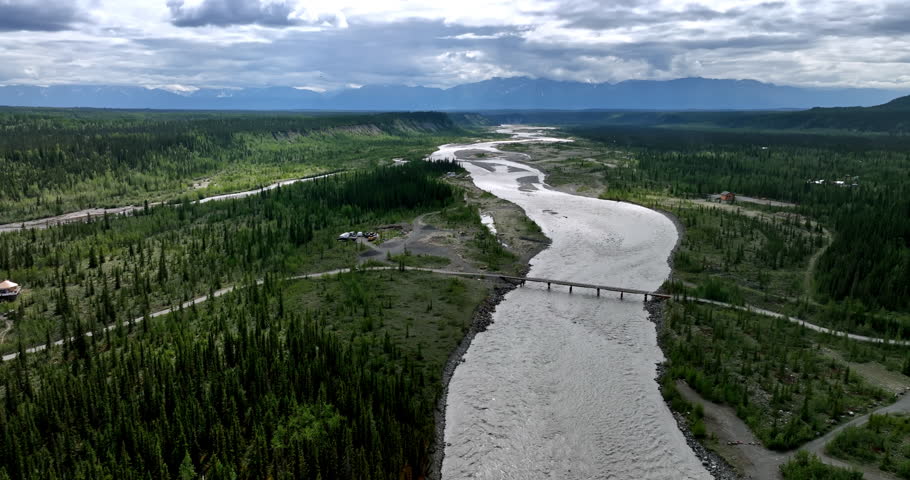 A car riding by the road approaches the bridge over the river. Aerial perspective on the vast nature landscape of Alaska, USA.