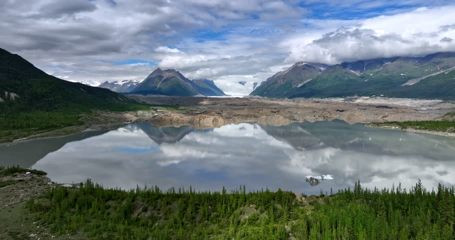 Beautiful mountains and grey clouds reflect in the lake. Ice melts in the valley of Alaska, USA. Aerial view.