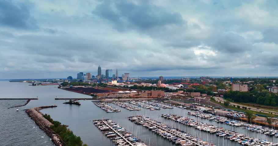 Numerous boats stand at the berths in the yacht club of Cleveland, Ohio, USA. City panorama under the grey overcast sky from drone footage.