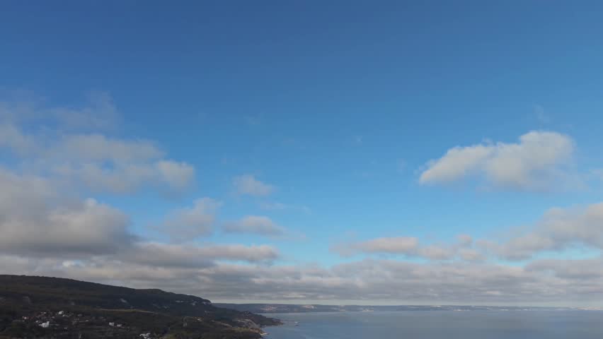 Aerial view of a dramatic coastline with clouds drifting across the sky. The scenic perspective highlights the natural contrast between land, sea, and sky from above.