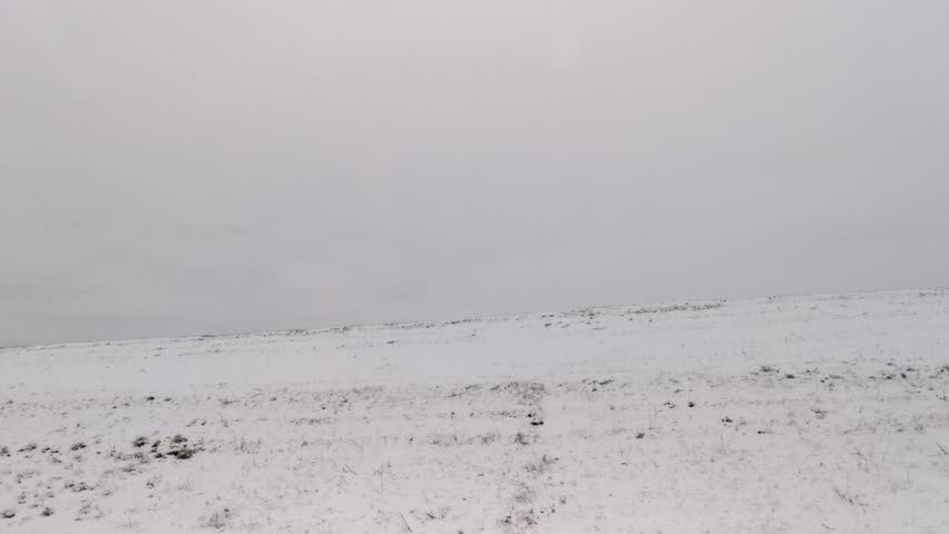 Snow field view from the car. The black earth is covered with snow. Fast traffic on the road. View from the side window of the car. The concept of traveling, driving along a country road. Winter day