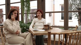 Two friends in a cafe one receives shocking news on a phone call reacting loudly while the other watches in fear covering her mouth tense atmosphere daylight emotional moment casual setting - Powered by Shutterstock - Get 15% off with code: PIKWIZARD15