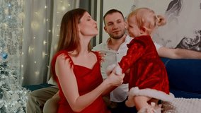 cozy living room mother plays with toddler; father watches from sofa, fairy lights and christmas tree in background, red dresses, warm smiles, intimate family bonding - Powered by Shutterstock - Get 15% off with code: PIKWIZARD15