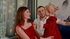 white family playing with toddler, joyful parents give high five to daughter in red dress near decorated tree and glowing string lights, warm holiday living room scene - Powered by Shutterstock - Get 15% off with code: PIKWIZARD15