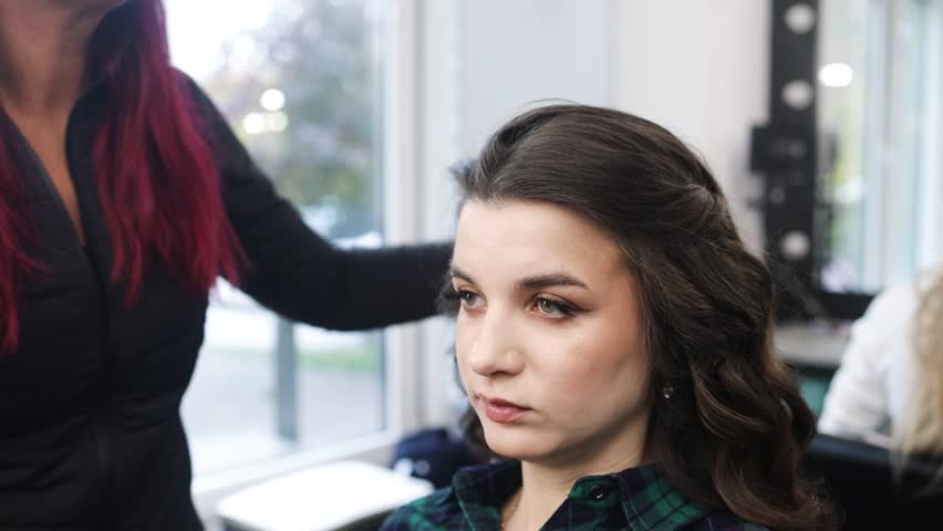 Hair stylist prepares woman makes curls hairstyle with curling iron.