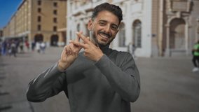 Smiling man in gray turtleneck showing fingers forming hashtag sign on street; digital connectivity. - Powered by Shutterstock - Get 15% off with code: PIKWIZARD15