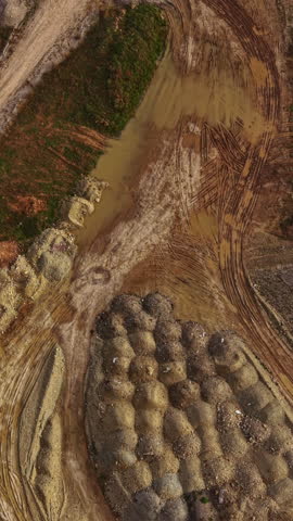 Wet earth spreads across a construction site where heavy machinery has left tracks. Piles of dirt and mud mingle with patches of green, showing early morning light.