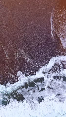 Early morning light reveals the gentle dance of waves meeting the shoreline, with white foam creating intricate patterns on the golden sand. A serene beach scene unfolds with nature