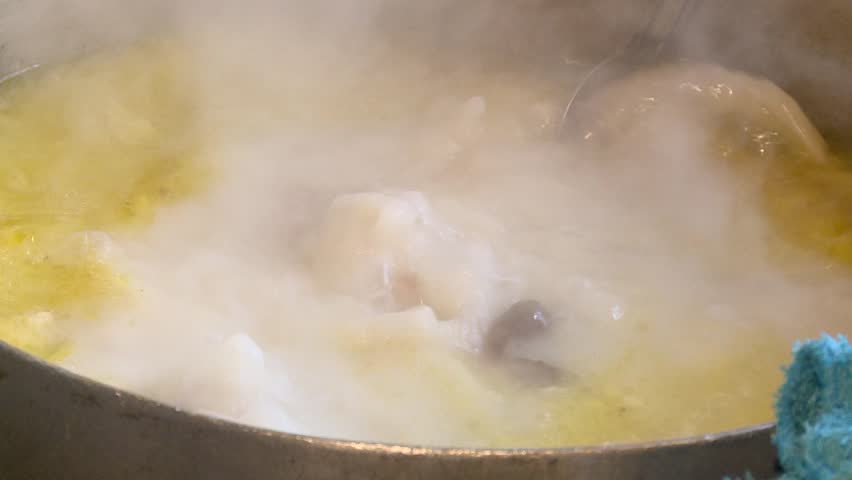 A large pot of hot, steaming soup or stew boils vigorously on the stovetop. A hand stirs the rich, yellow broth and meat chunks, creating a comforting culinary scene perfect for food-related projects.