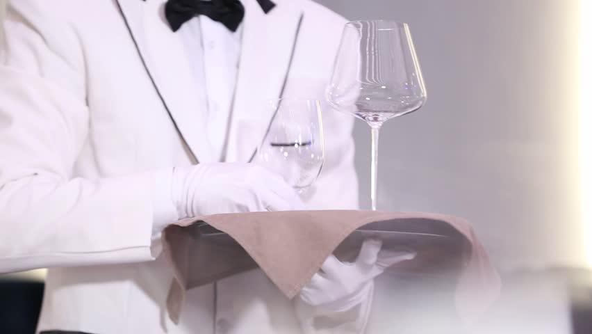 A detailed close-up shot captures a gloved hand meticulously arranging cutlery, a plate, and a dark napkin on a beautifully set white table. Perfect for showcasing professional event preparation.