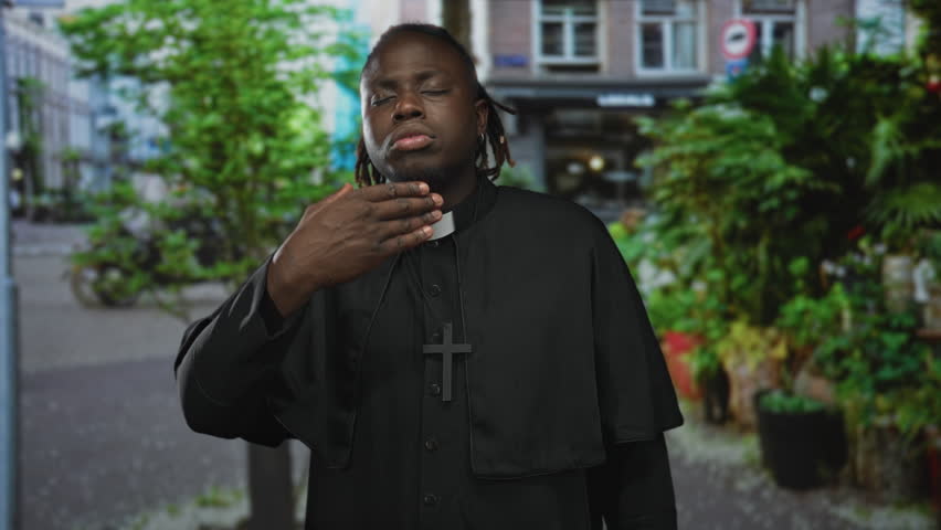 Priest man with clerical collar and wooden cross holds arms outstretched and eyes closed while standing on a city street lined with planters; faith serenity.