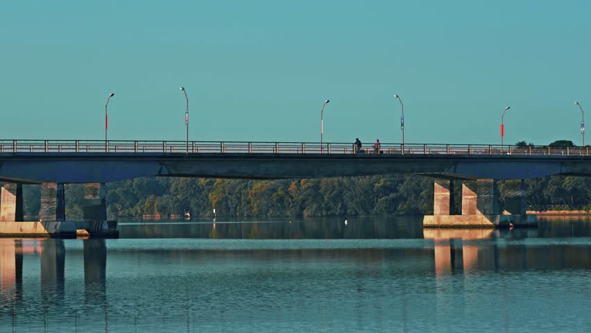 long-distance shot of a small bridge over the blue waters of a lake in the early hours of the morning