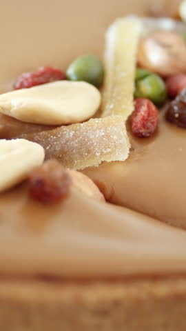 Caramel tart slice with nuts and dried fruits on biscuit base shown in macro with glossy caramel surface dripping over crust
