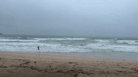Stormy sea with large, powerful waves crashing on a sandy beach. Red warning flag indicating dangerous swimming conditions during bad weather - Powered by Shutterstock - Get 15% off with code: PIKWIZARD15