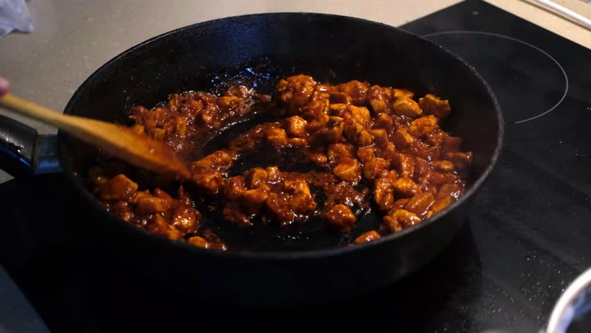 Stirring spicy chicken in a pan for a flavorful cooking experience