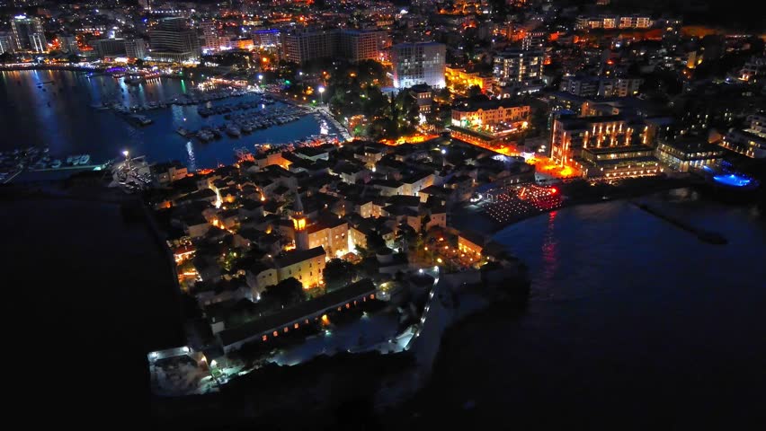 Night city with electric lights against the backdrop of slopes of the Montenegrin mountains and the starry sky near the Adriatic Sea