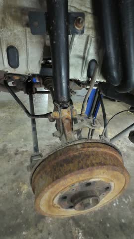 Mechanic inspecting rusted brake components, Closeup of corroded automotive brake assembly, Industrial workshop environment with mechanic examining aged and damaged brake parts on vehicle