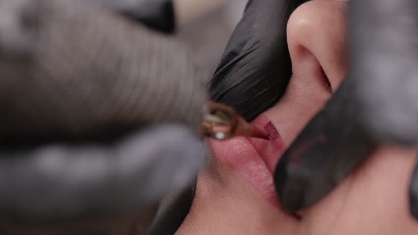 Macro video process of applying microblading permanent makeup tattoo of red on lips woman.